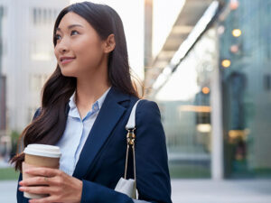 コーヒーを片手にオフィス街にたたずむ女性