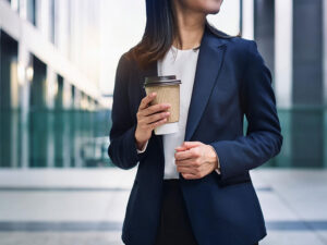 コーヒーを片手にオフィス街にたたずむ女性