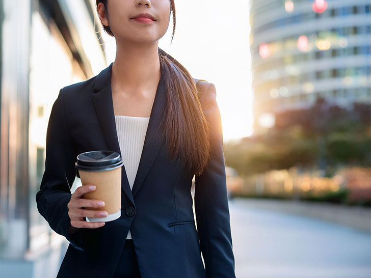 コーヒーを片手にオフィス街にたたずむ女性