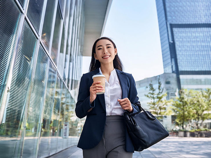 コーヒーを片手にオフィス街にたたずむ女性