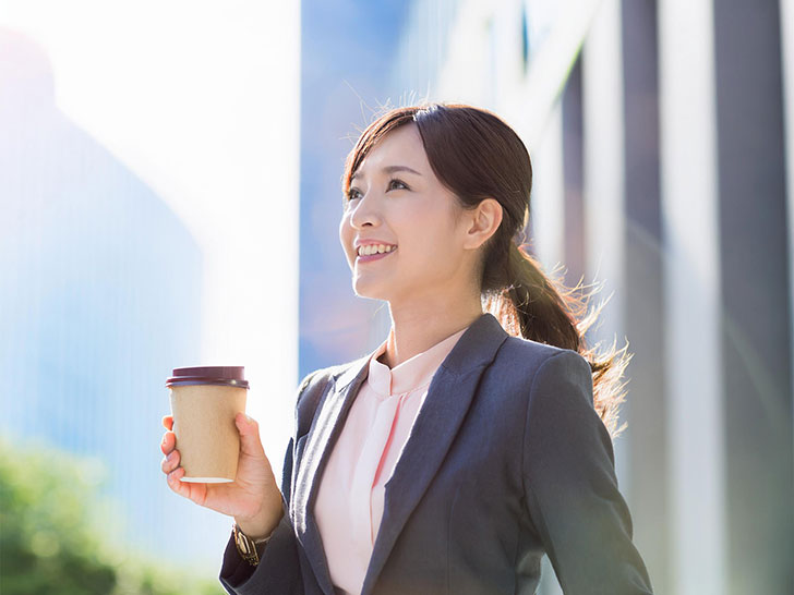 コーヒーを片手にオフィス街にたたずむ女性