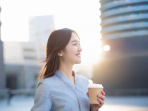 コーヒーを片手にオフィス街にたたずむ女性