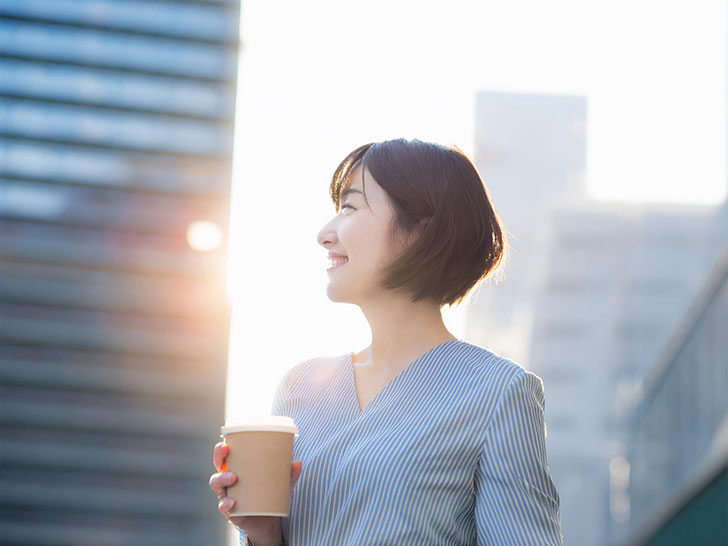 コーヒーを片手にオフィス街にたたずむ女性