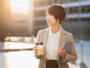 コーヒーを片手にオフィス街にたたずむ女性