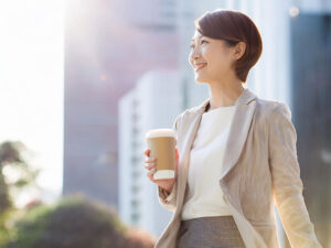 コーヒーを片手にオフィス街にたたずむ女性