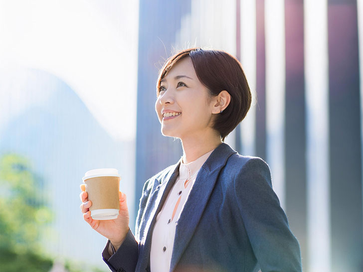 コーヒーを片手にオフィス街にたたずむ女性