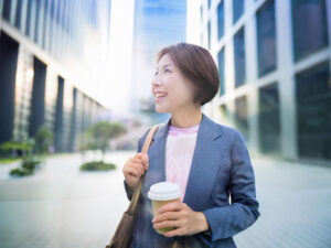 コーヒーを片手にオフィス街にたたずむ女性