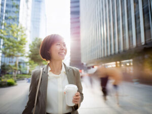 コーヒーを片手にオフィス街にたたずむ女性