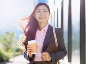 コーヒーを片手にオフィス街にたたずむ女性