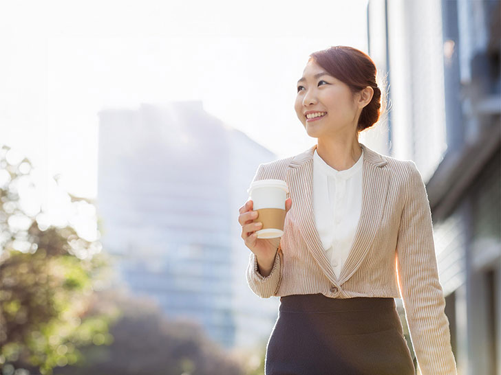 コーヒーを片手にオフィス街にたたずむ女性