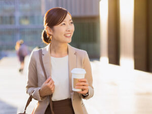 コーヒーを片手にオフィス街にたたずむ女性