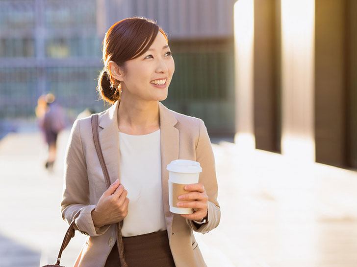 コーヒーを片手にオフィス街にたたずむ女性