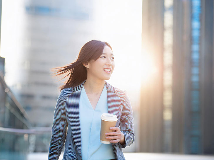 コーヒーを片手にオフィス街にたたずむ女性