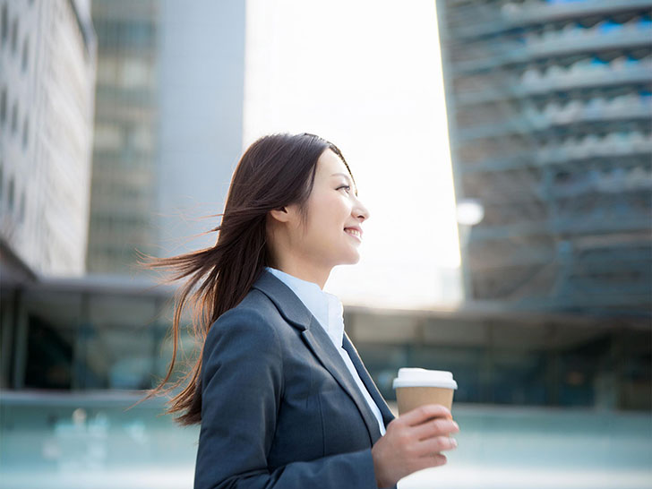 コーヒーを片手にオフィス街にたたずむ女性