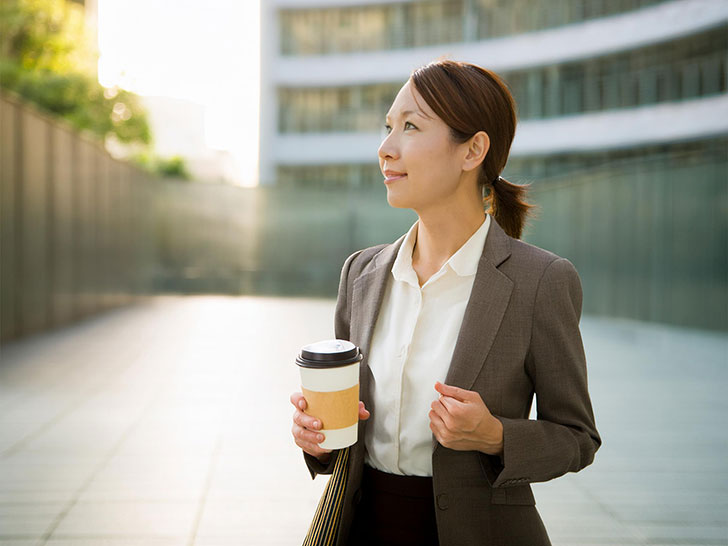 コーヒーを片手にオフィス街にたたずむ女性