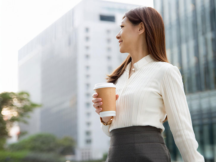 コーヒーを片手にオフィス街にたたずむ女性