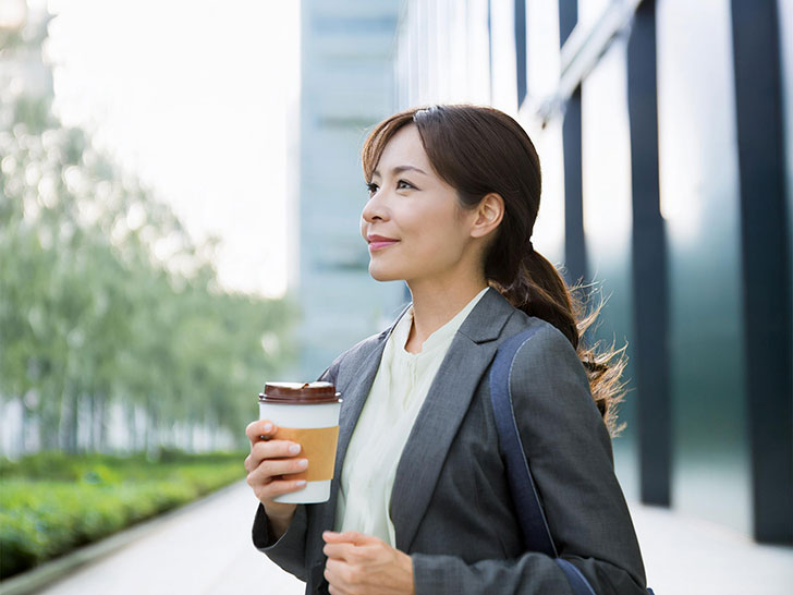 コーヒーを片手にオフィス街にたたずむ女性