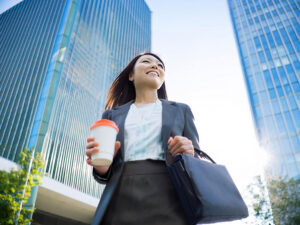 コーヒーを片手にオフィス街にたたずむ女性