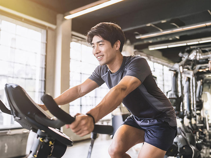 スポーツジムでエアロバイクをこぐ男性