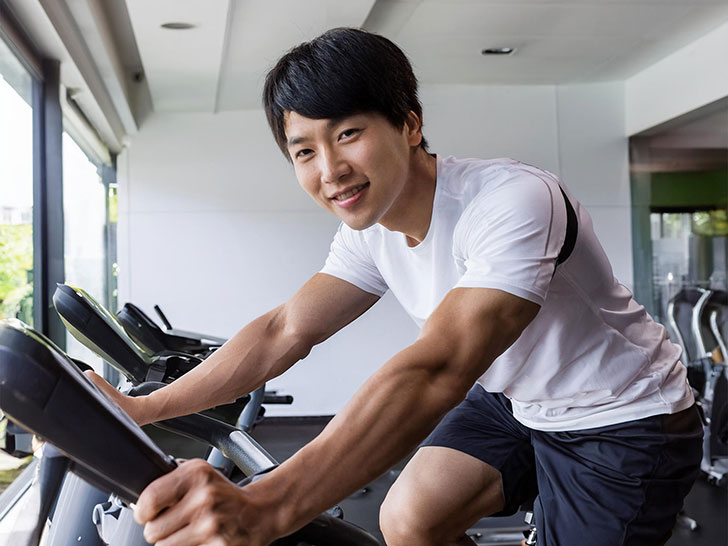 スポーツジムでエアロバイクをこぐ男性