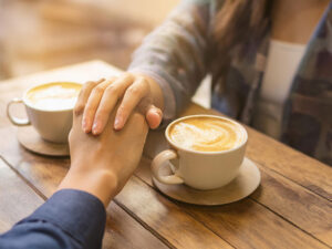 カフェラテの前で重ねられたカップルの手