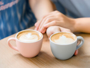 カフェラテの前で重ねられたカップルの手