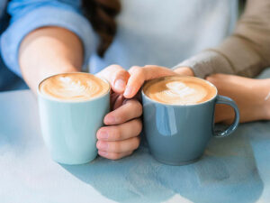 カフェラテの前で重ねられたカップルの手