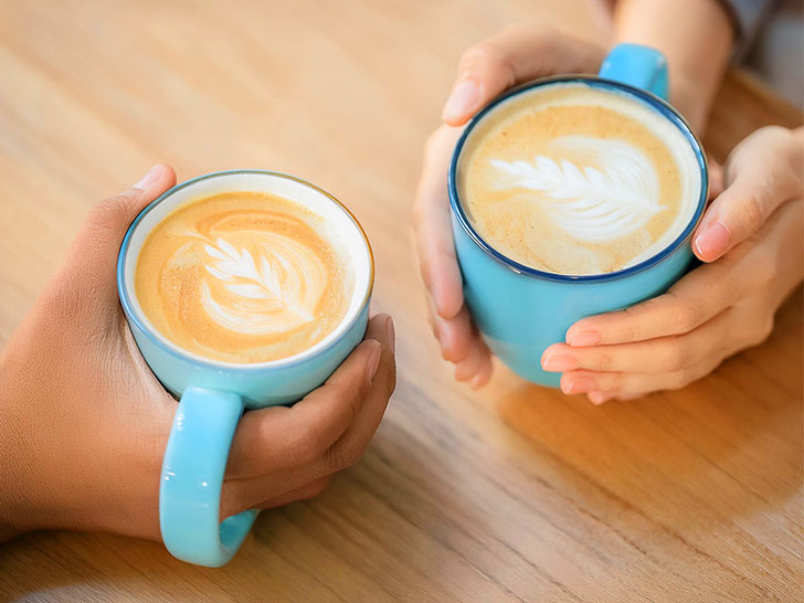 カフェラテの前で重ねられたカップルの手