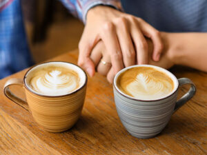 カフェラテの前で重ねられたカップルの手