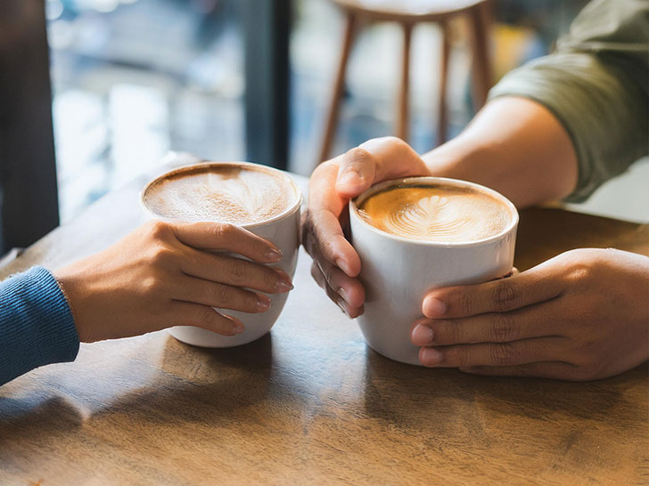 カフェラテの前で重ねられたカップルの手