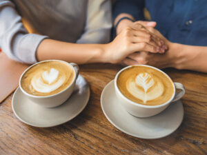 カフェラテの前で重ねられたカップルの手