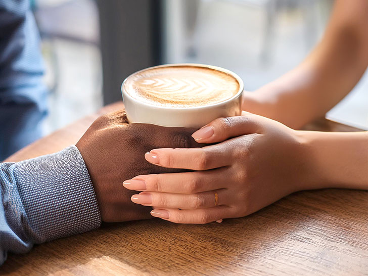 カフェラテの前で重ねられたカップルの手