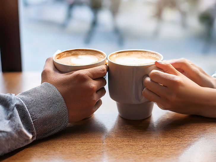 カフェラテの前で重ねられたカップルの手