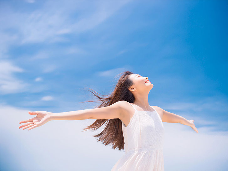 青空に向かって両手を広げる若い女性