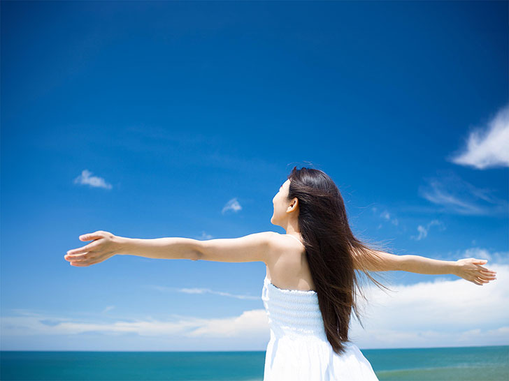 青空に向かって両手を広げる若い女性