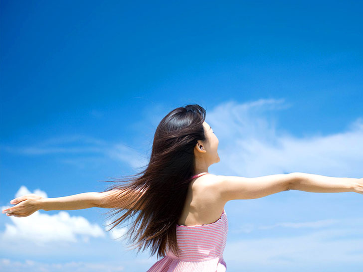 青空に向かって両手を広げる若い女性