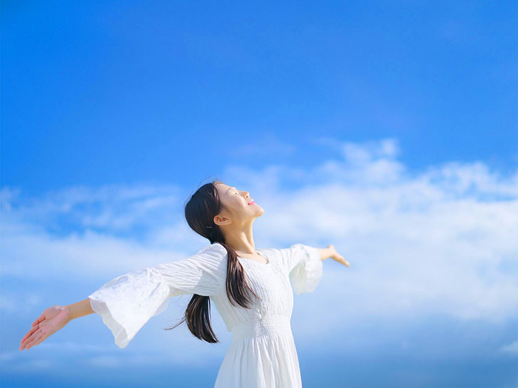 青空に向かって両手を広げる若い女性