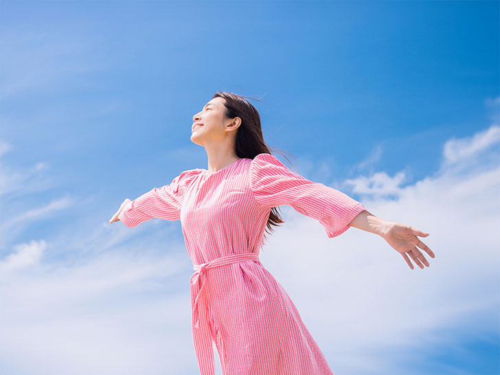 青空に向かって両手を広げる若い女性