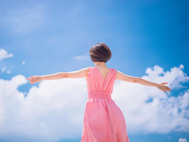 青空に向かって両手を広げる若い女性