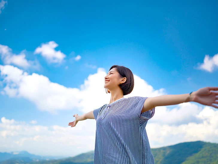 青空に向かって両手を広げる若い女性