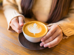 カフェラテのマグカップを持つ女性の手