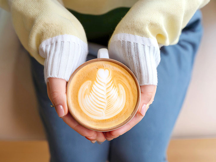 カフェラテのマグカップを持つ女性の手