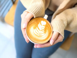 カフェラテのマグカップを持つ女性の手