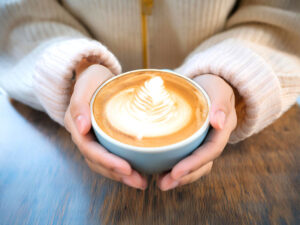 カフェラテのマグカップを持つ女性の手