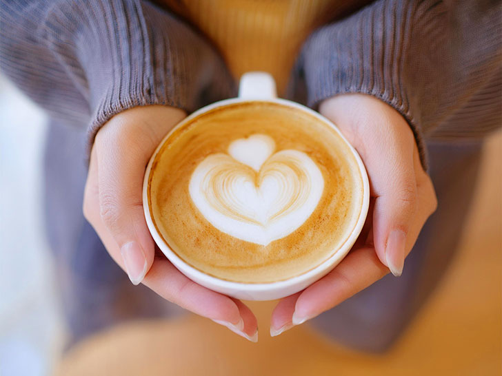 カフェラテのマグカップを持つ女性の手