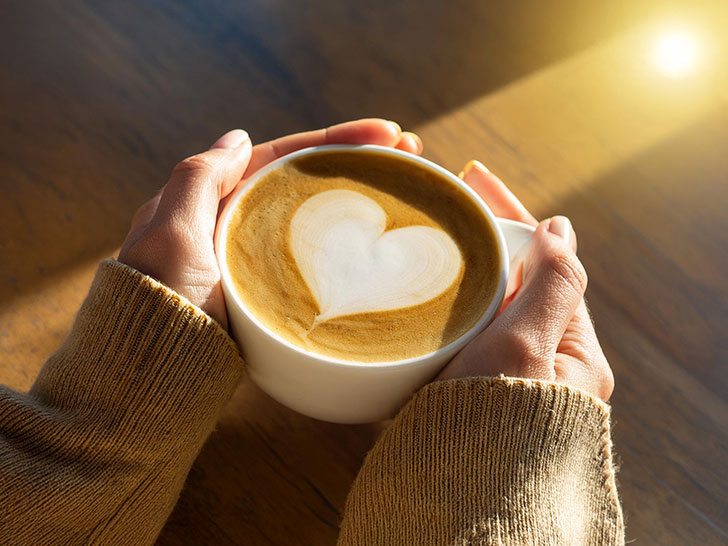 カフェラテのマグカップを持つ女性の手