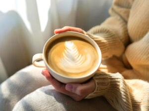 カフェラテのマグカップを持つ女性の手