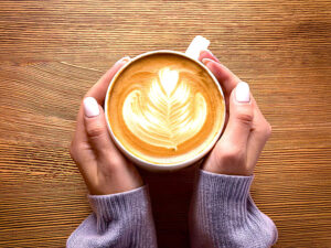 カフェラテのマグカップを持つ女性の手