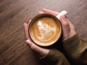 カフェラテのマグカップを持つ女性の手