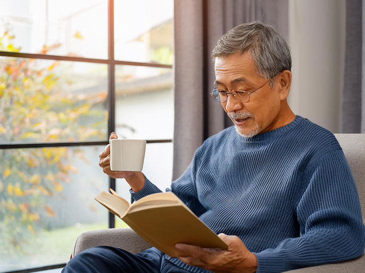 コーヒーを飲みながら読書をするシニア男性